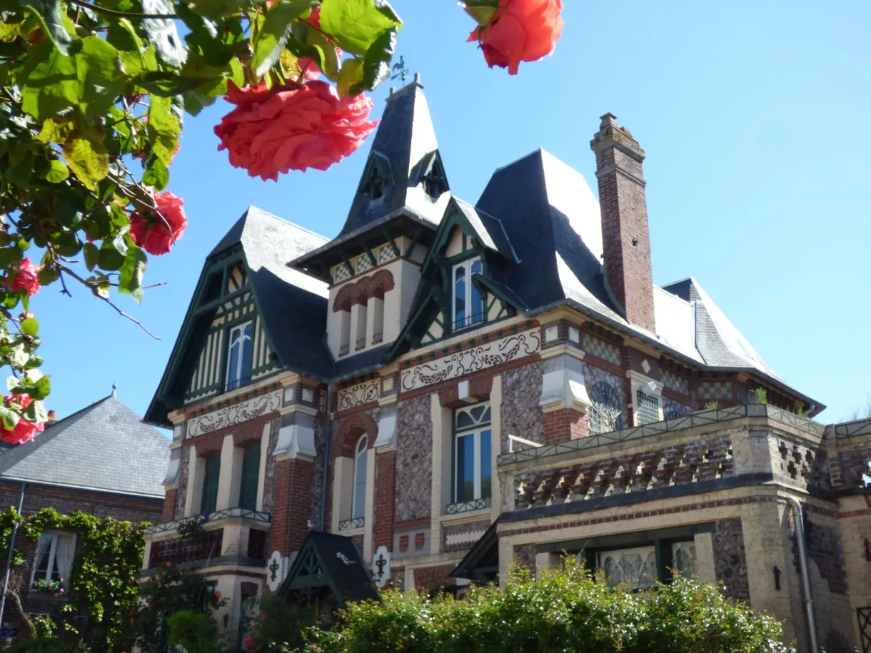 Villa balnéaire à tourelles derrière un rosier rouge en fleurs