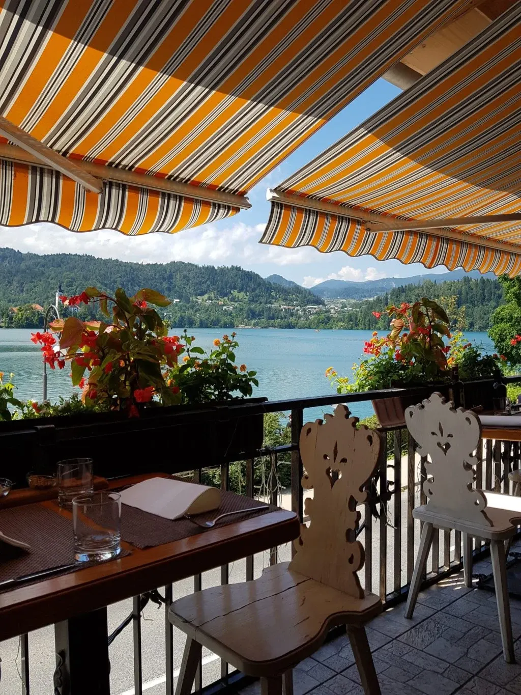 Terrasse fleurie sous un store rayé face au lac