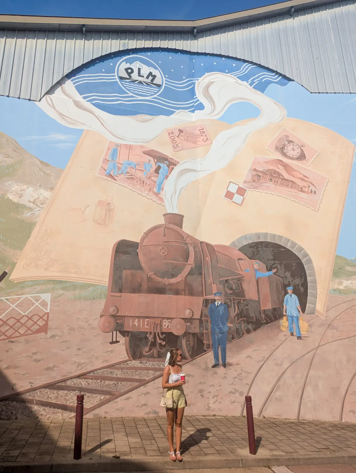 Fresque murale d'une locomotive à vapeur devant laquelle pose une visiteuse