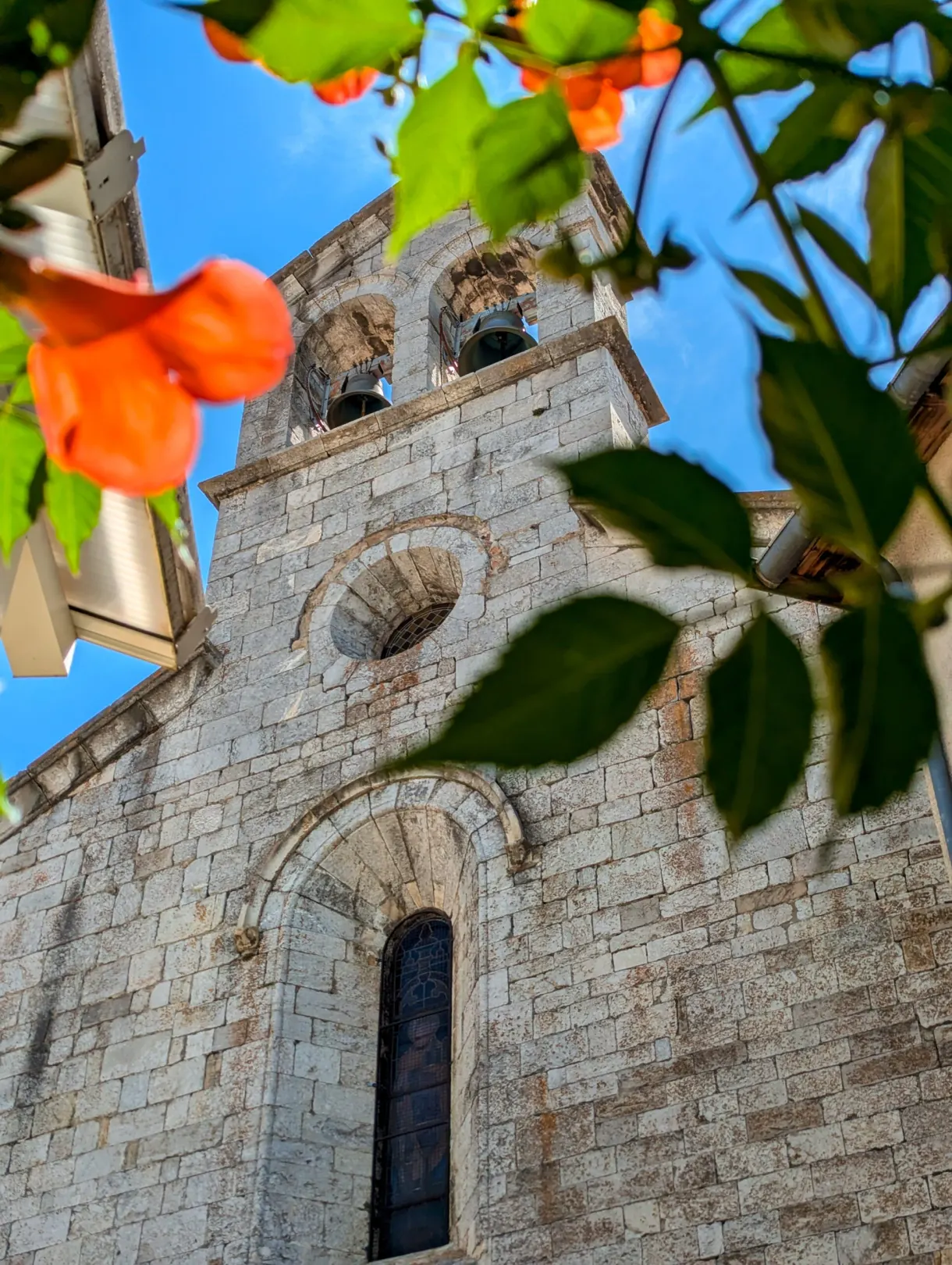 Clocher de pierre aperçu entre les feuillages et des fleurs orangées