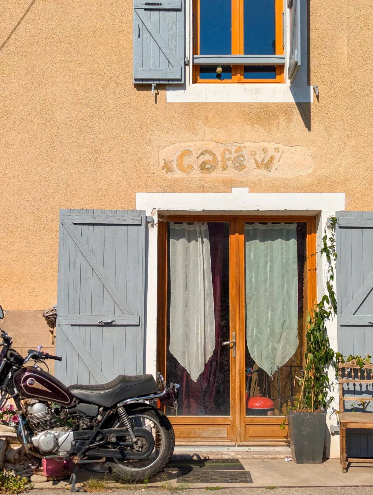 Ancienne enseigne de café peinte sur une façade ocre, moto garée devant