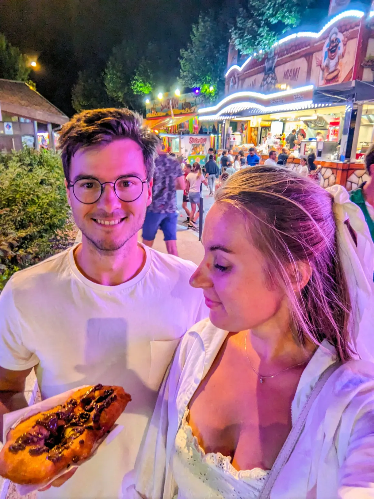 Couple partageant une pâtisserie devant les stands illuminés de la fête