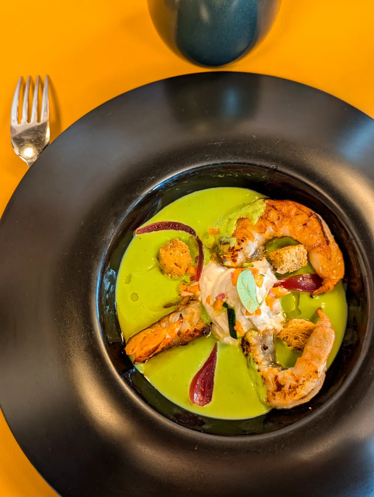 Crevettes poêlées et velouté vert servis dans une assiette creuse noire
