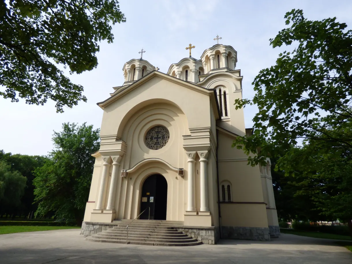 Église orthodoxe crème à trois coupoles entourée d'arbres