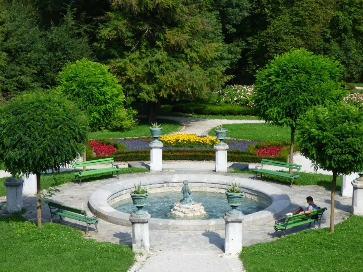 Bassin rond et parterres fleuris entre les bancs verts