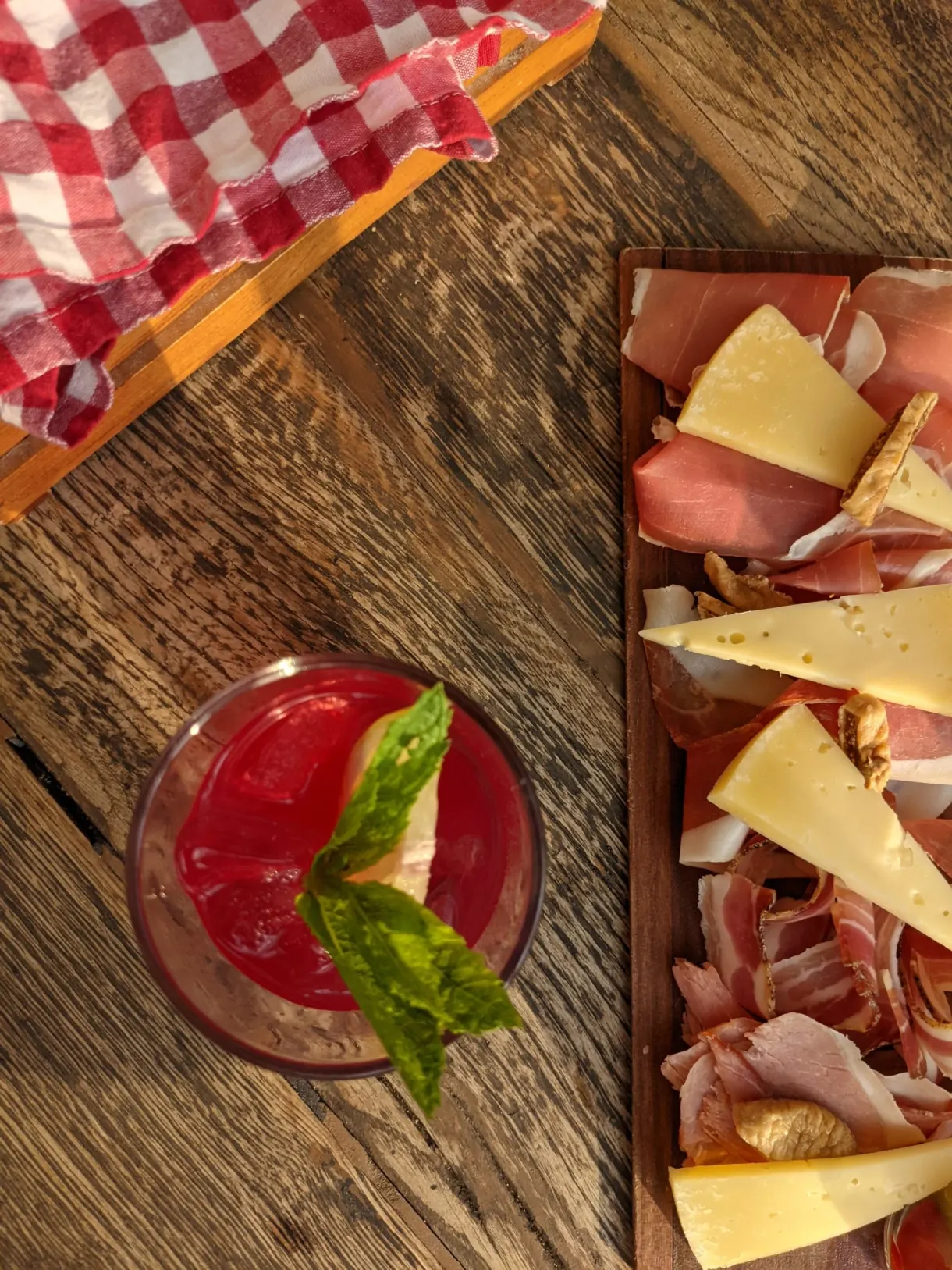 Planche de charcuterie et fromages avec cocktail rouge sur bois brut