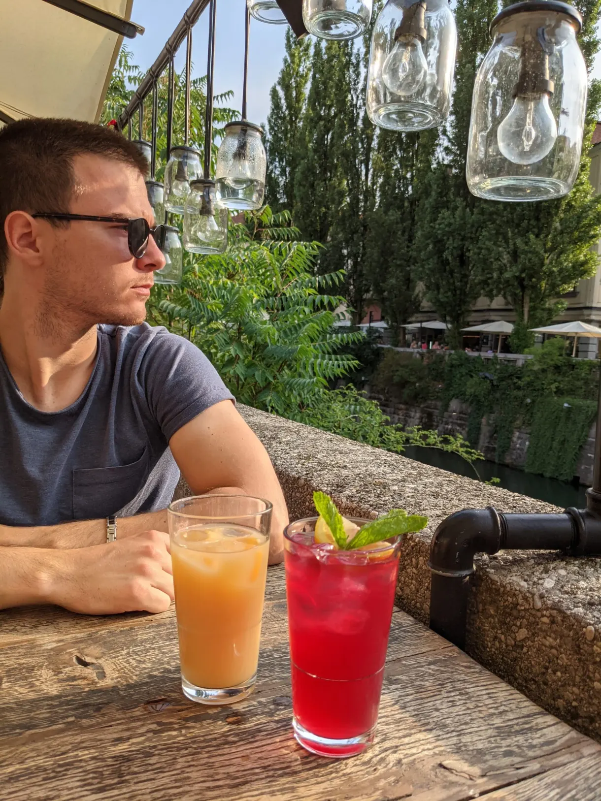 Homme accoudé à une terrasse au bord de l'eau, deux cocktails