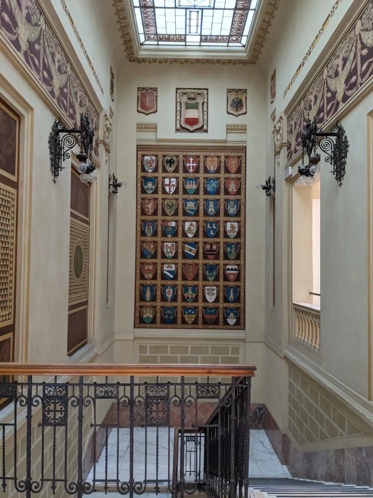 Blasons peints alignés au-dessus d'un escalier à rampe de fer