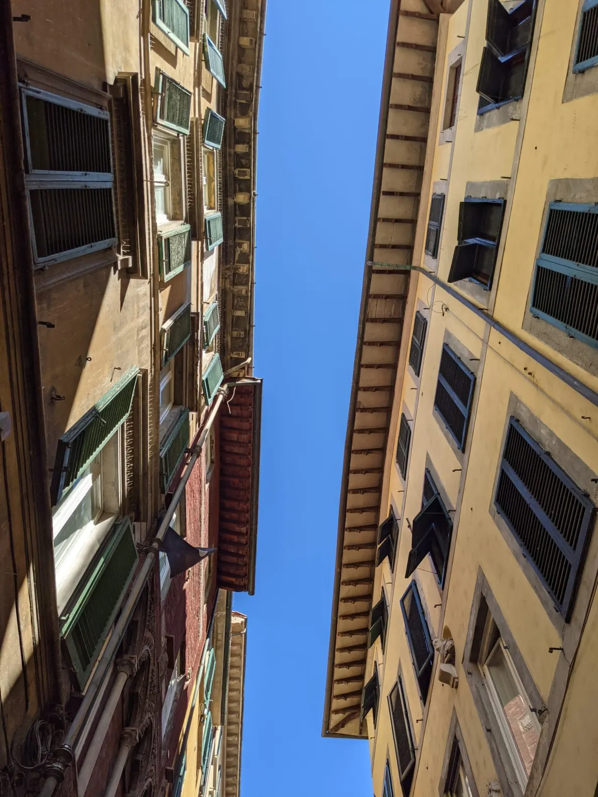 Bande de ciel étroite entre deux façades aux volets verts