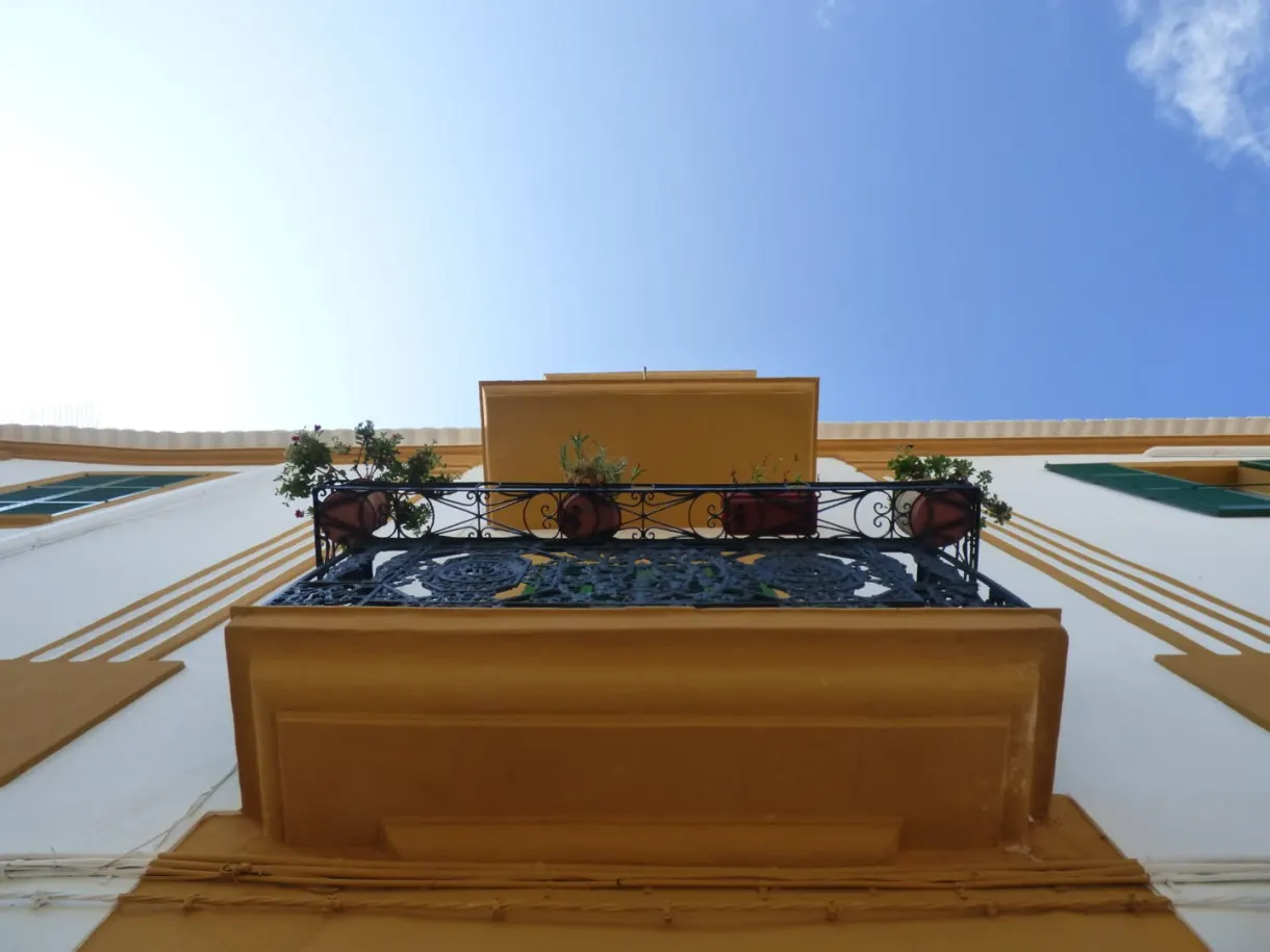Balcon ocre chargé de pots de fleurs en contre-plongée