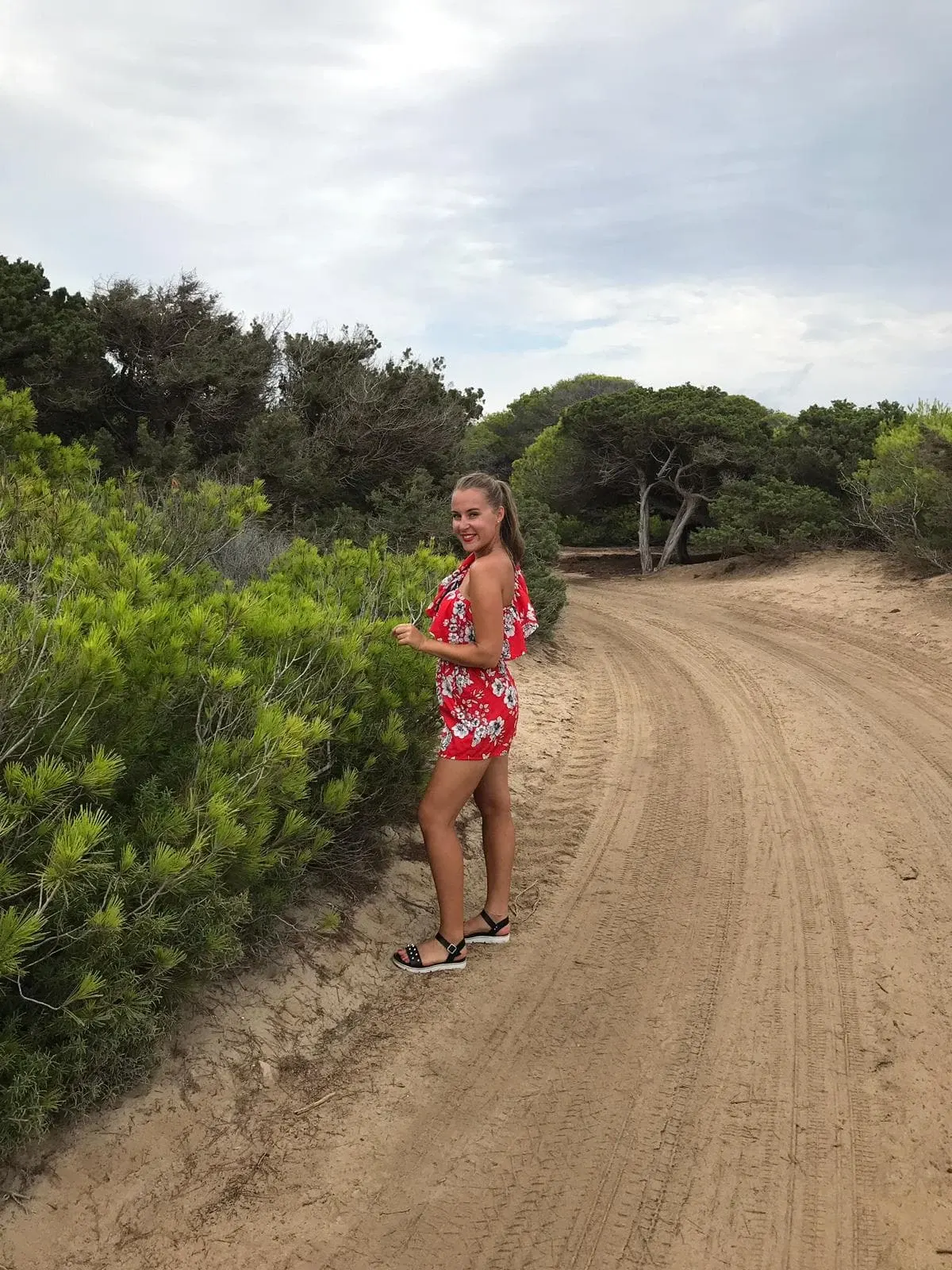 Marcheuse en robe rouge sur un chemin de sable bordé de pins