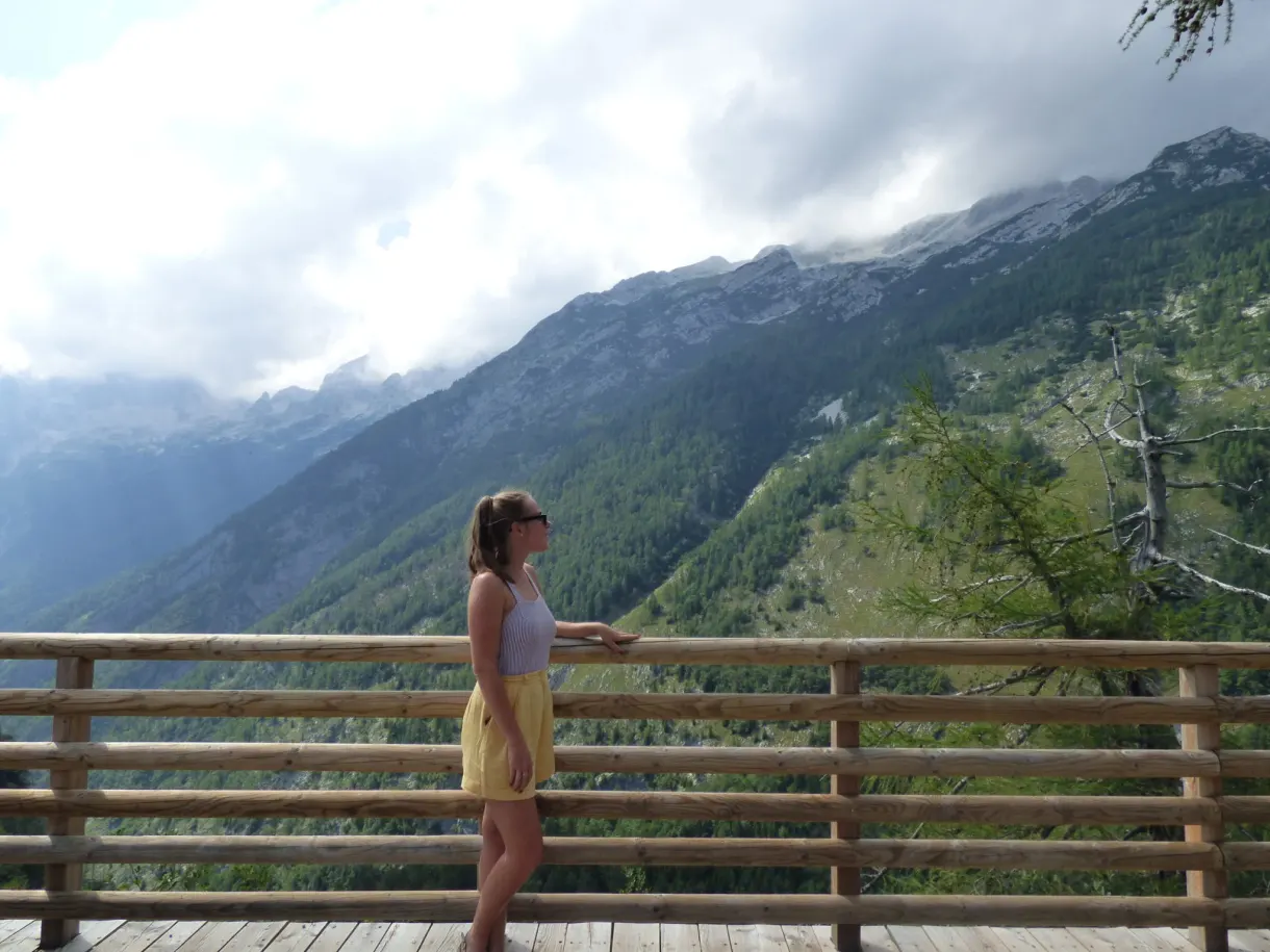 Femme accoudée à une rambarde de bois face à la vallée