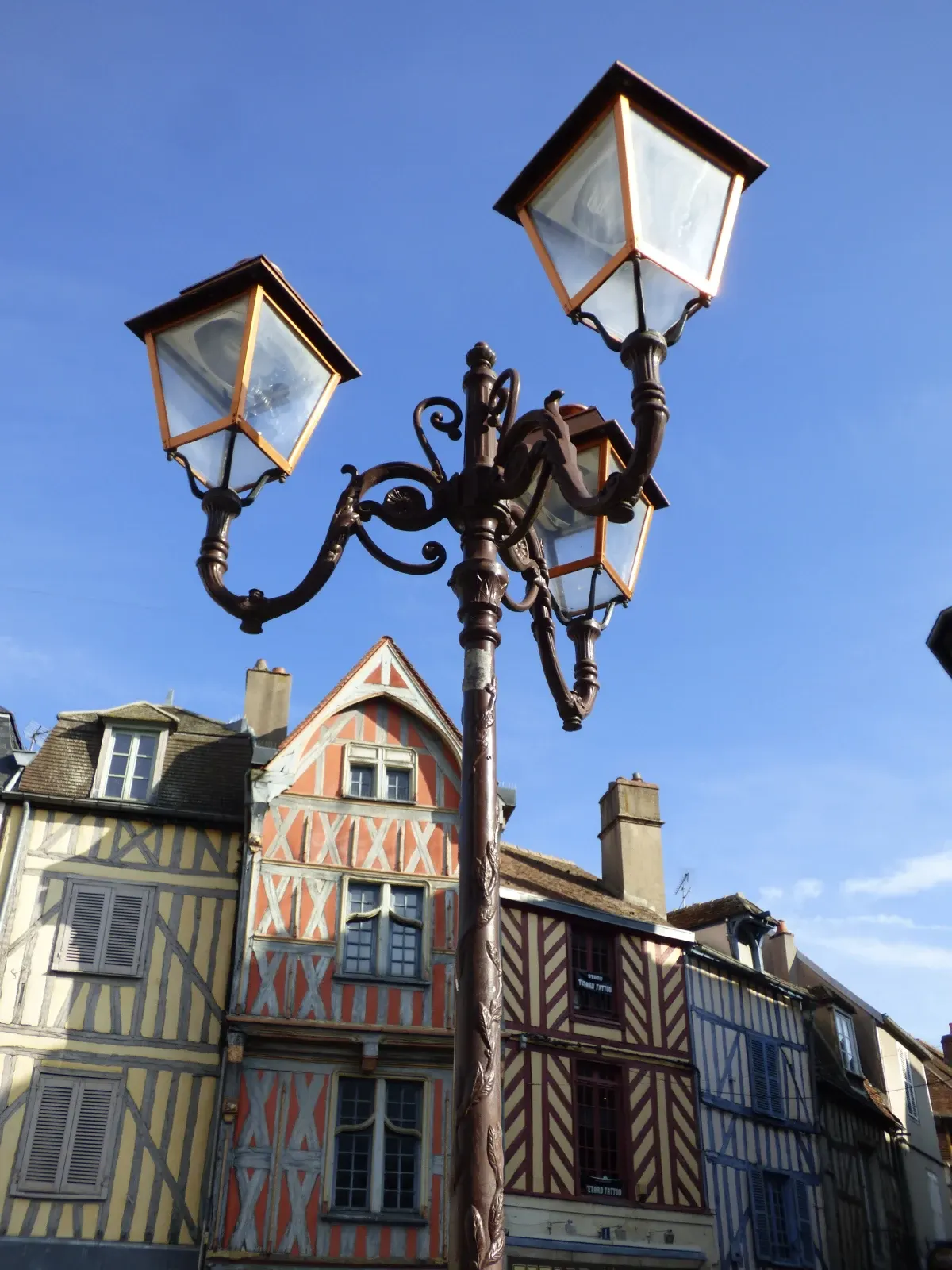 Lampadaire ouvragé devant des maisons à colombages d'Auxerre