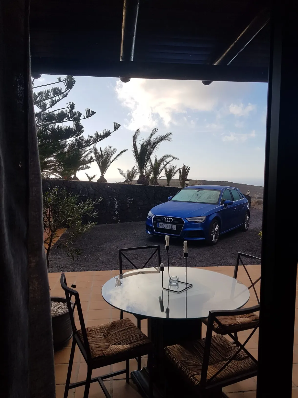 Terrasse abritée avec table ronde et voiture bleue garée devant