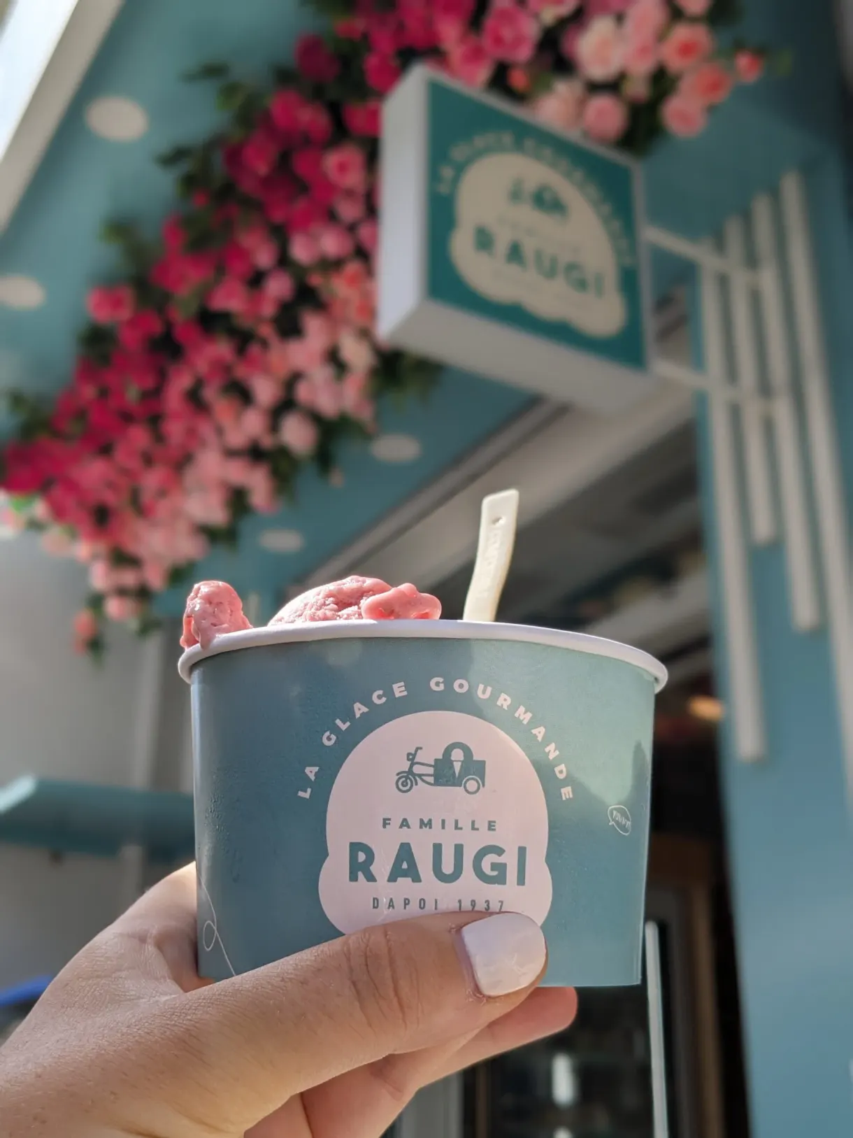 Pot de glace tenu devant une devanture turquoise fleurie