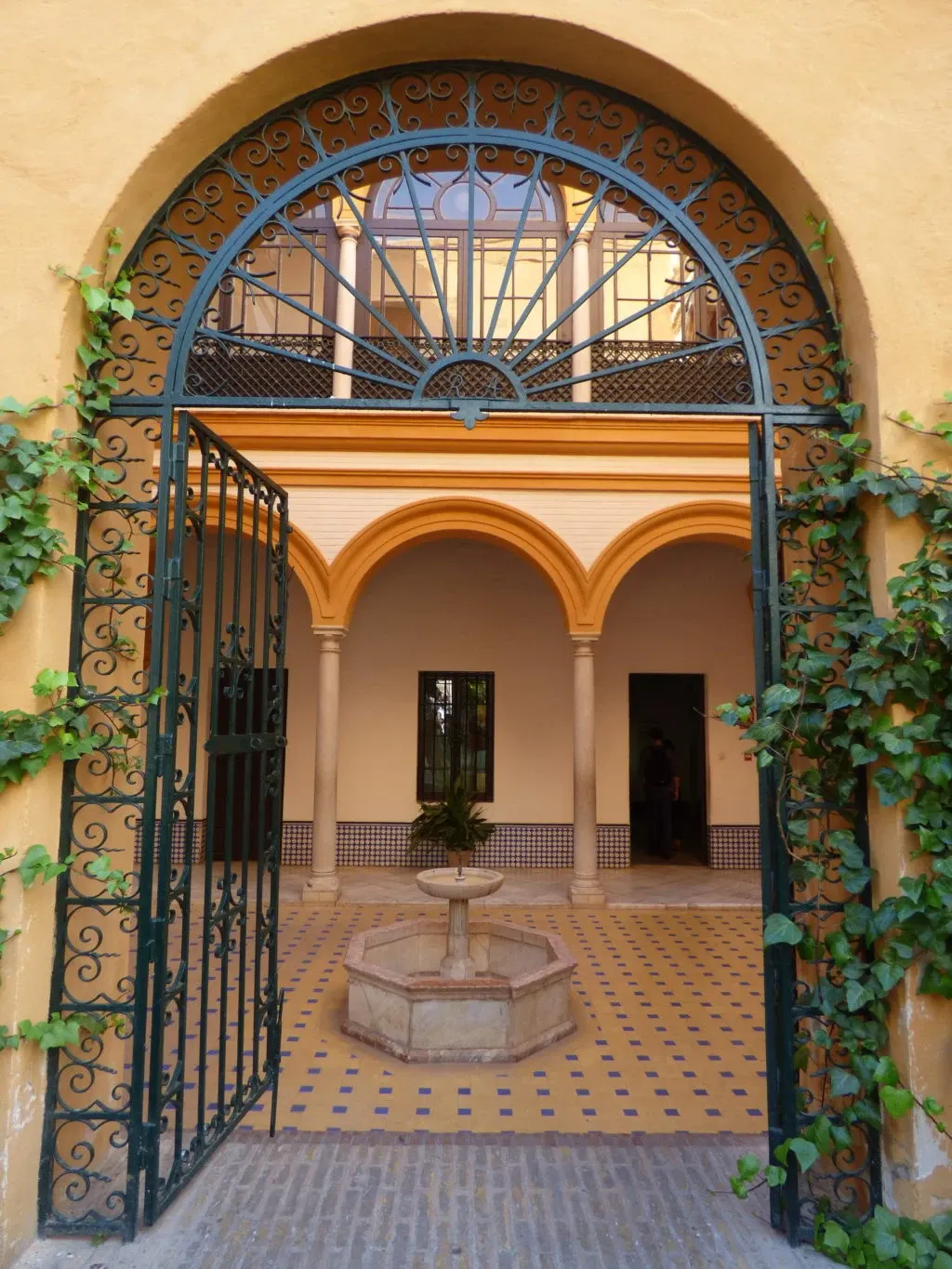 Grille ouvragée ouvrant sur un patio à fontaine et arcades