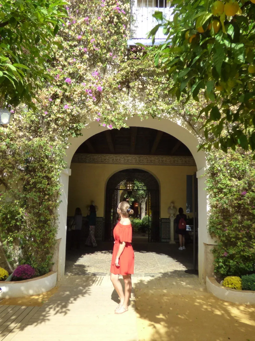 Femme en robe rouge sous un porche fleuri de bougainvillier