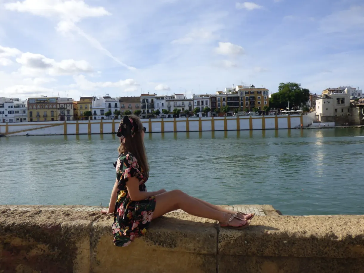 Femme assise sur un muret face au fleuve et aux maisons