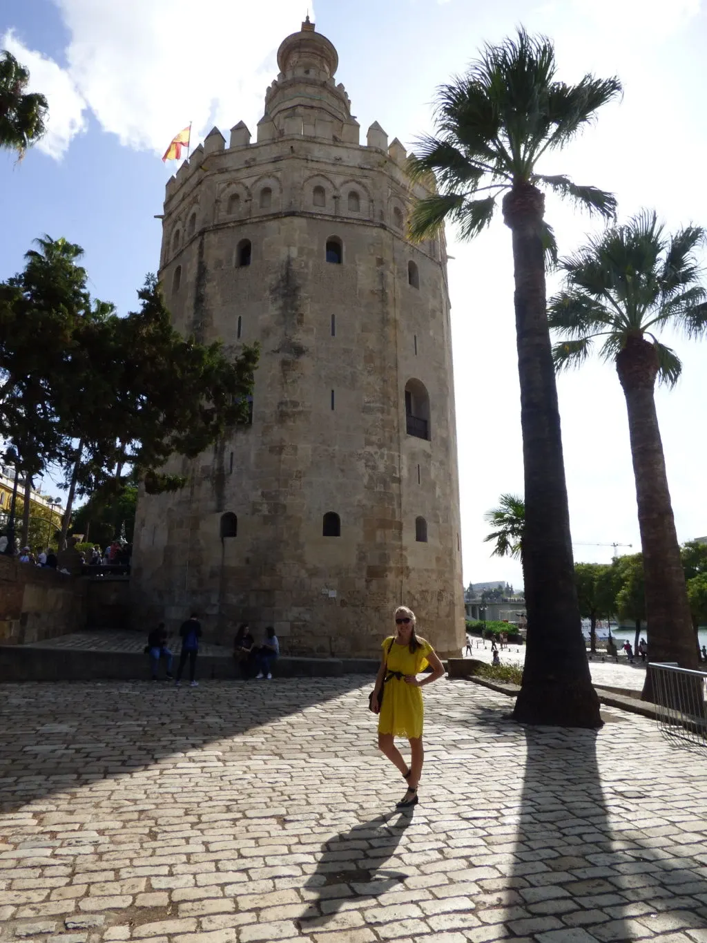 Femme en robe jaune devant la tour dorée et deux palmiers