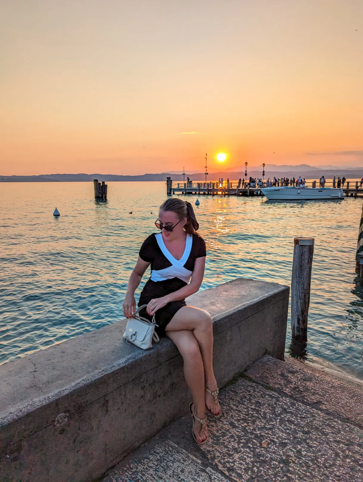 Femme assise sur un muret face au soleil couchant