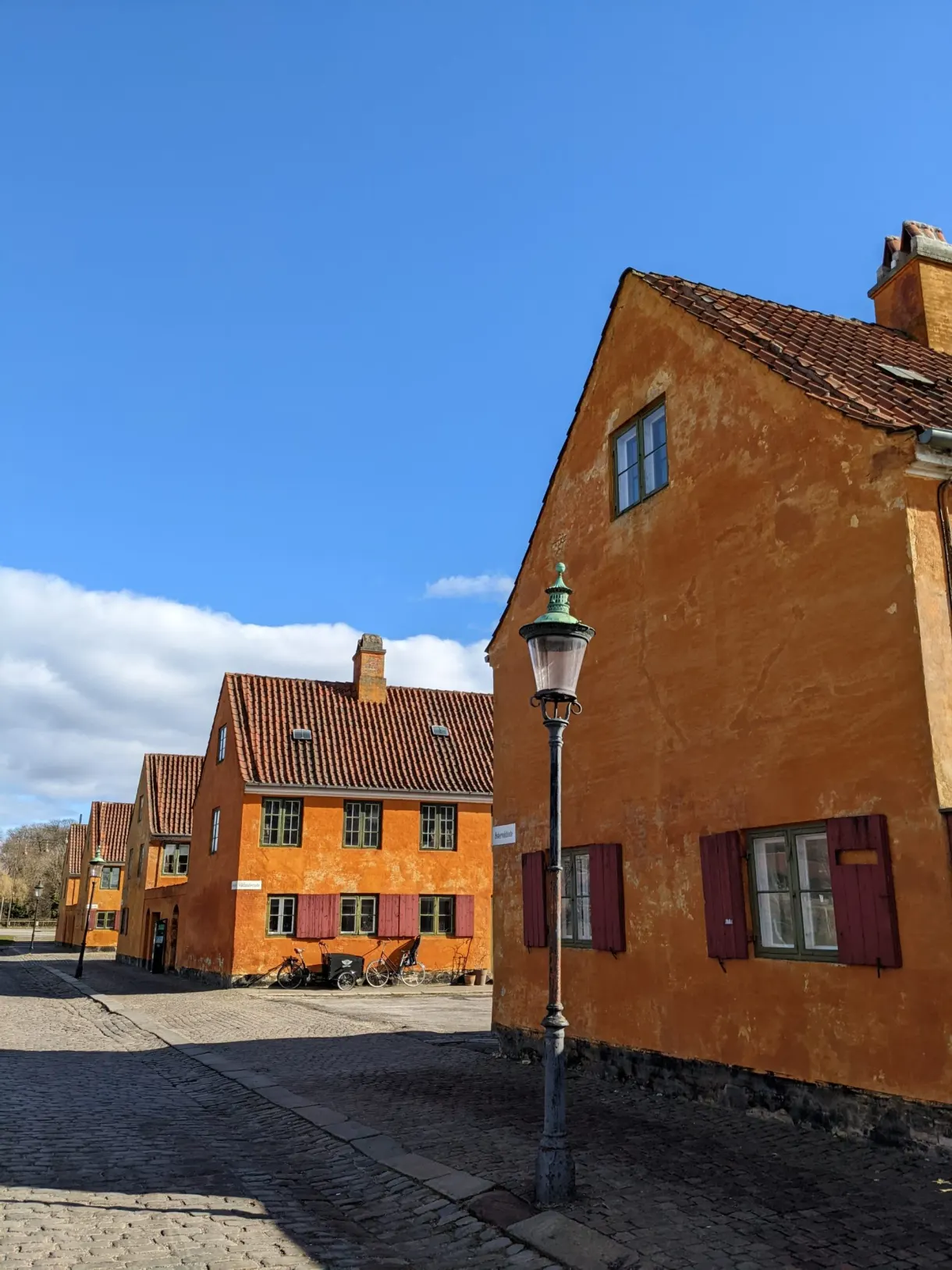 Réverbère au coin d'une maison ocre, rue pavée en enfilade