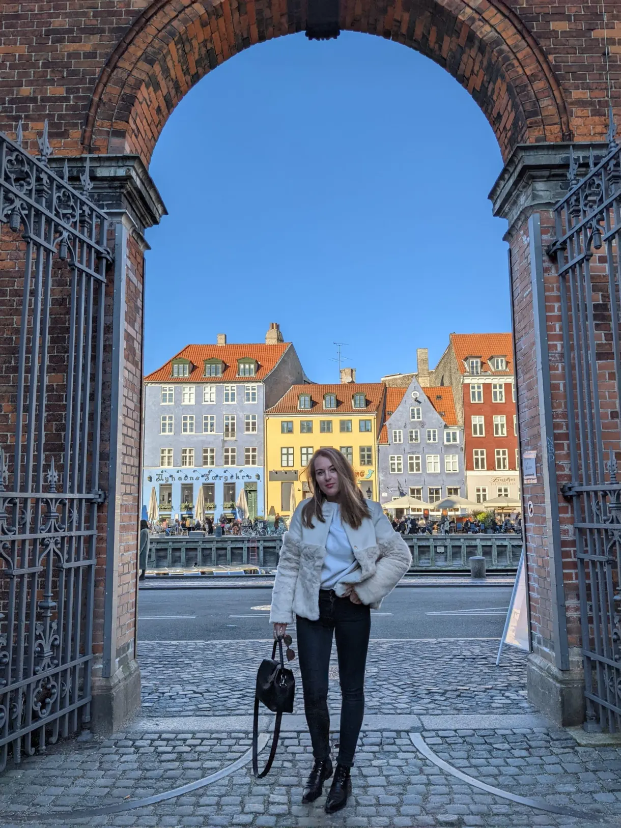 Voyageuse sous une arche de brique face aux maisons de Nyhavn