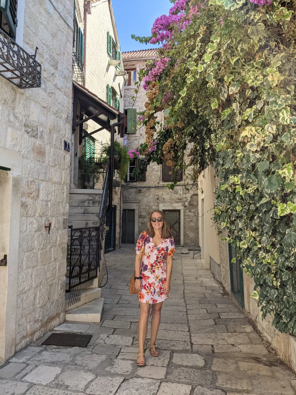 Femme en robe fleurie dans une ruelle pavée bordée de bougainvillier