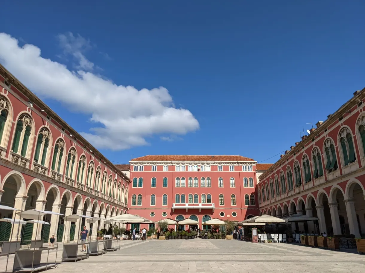 Grande place bordée d'arcades rouges sous un ciel bleu