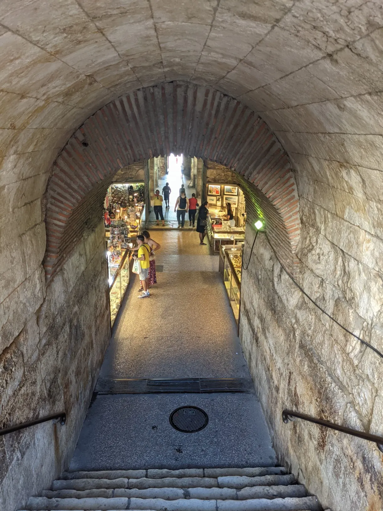 Passage voûté et escalier descendant vers des échoppes éclairées