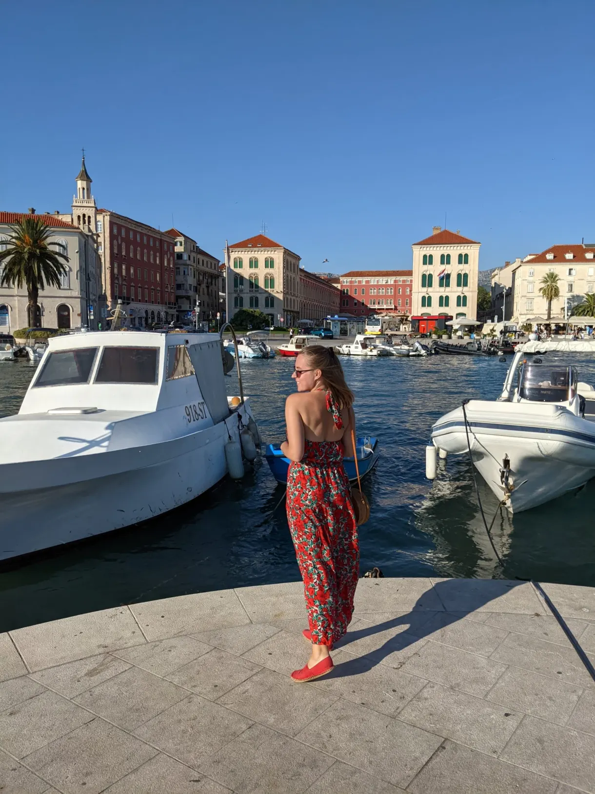 Femme en robe rouge entre deux bateaux à quai