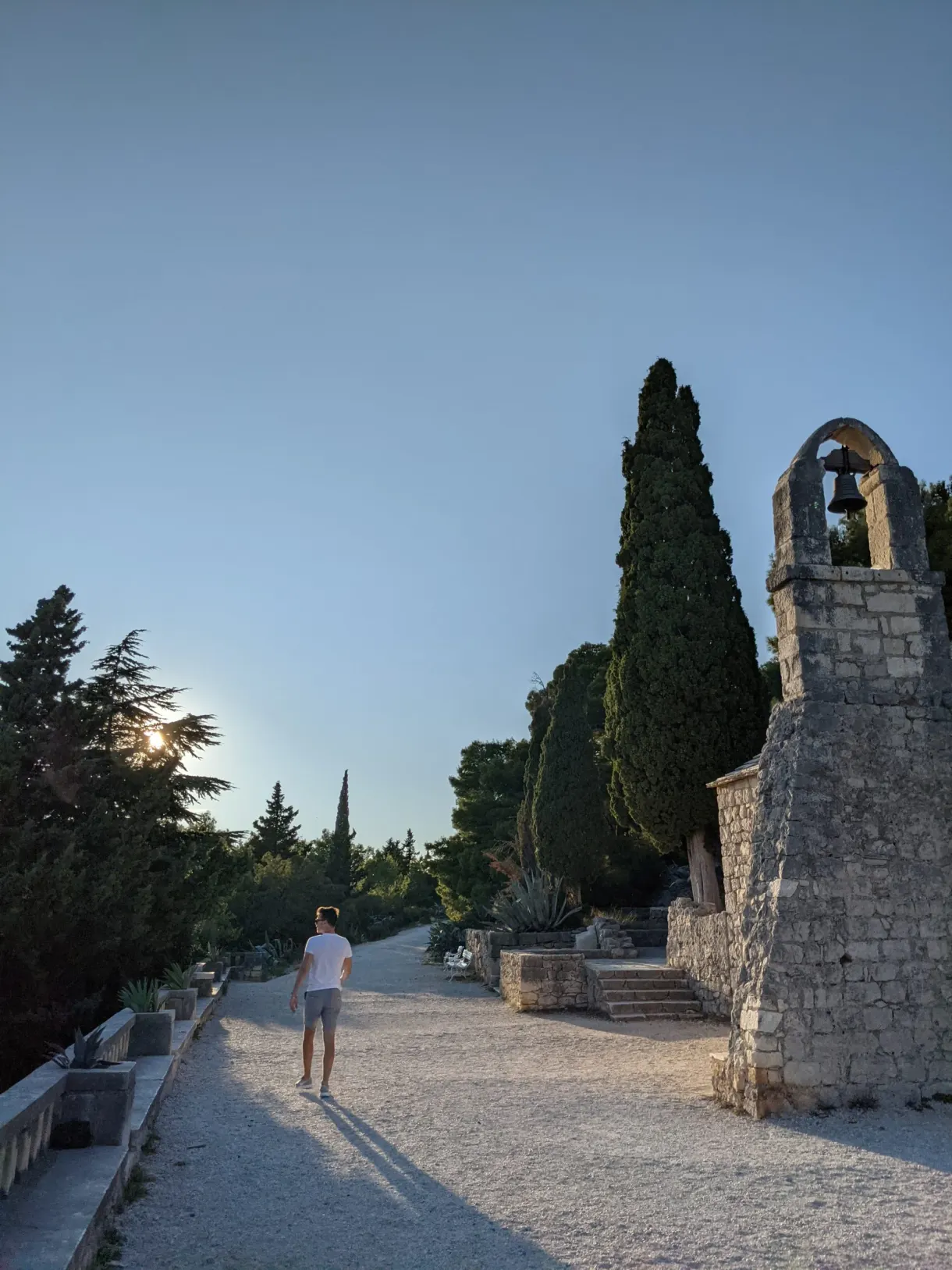 Allée de gravier menant à une chapelle de pierre entre les cyprès