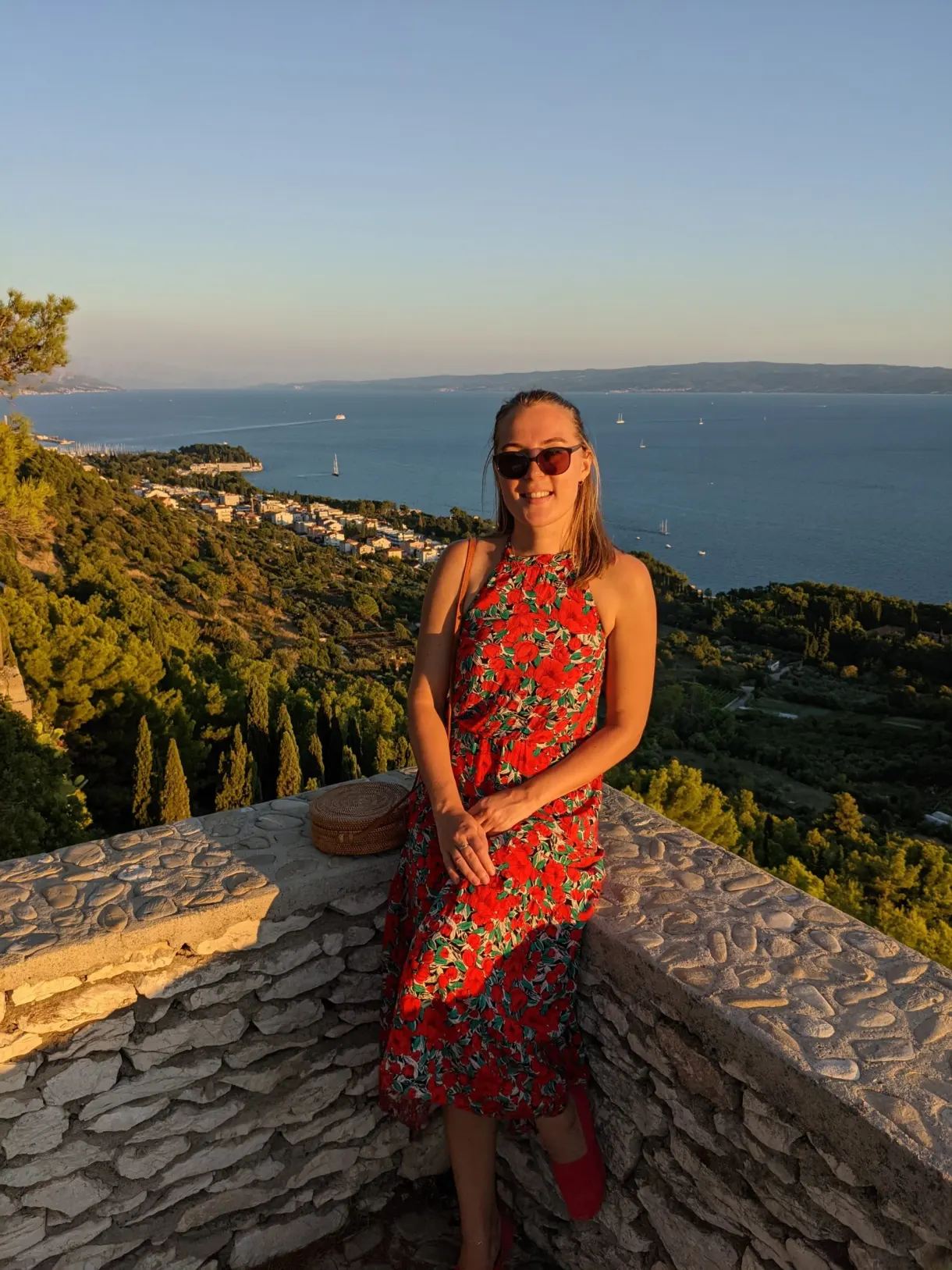 Femme en robe fleurie assise sur un muret face au large