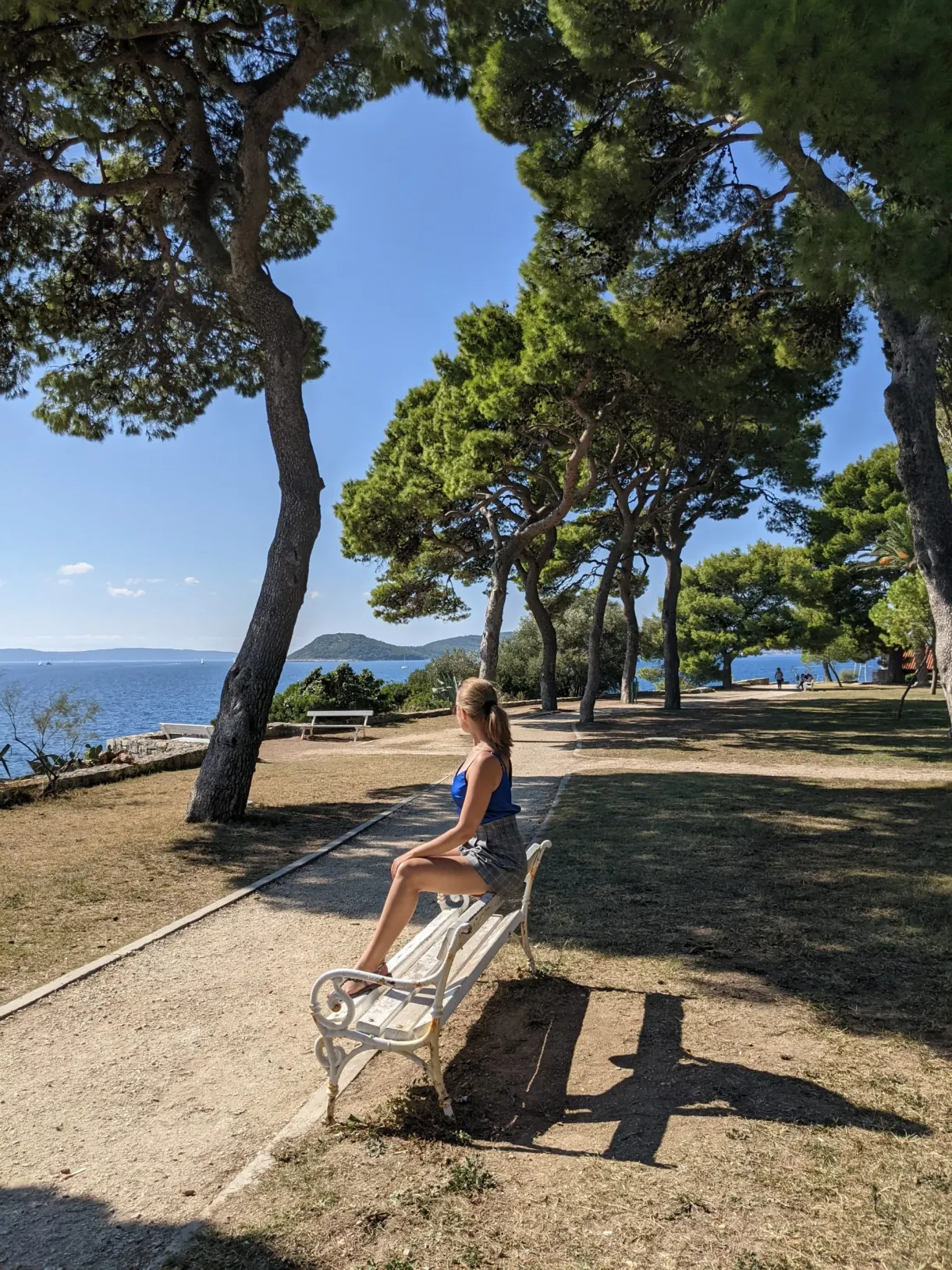 Femme assise sur un banc blanc sous les pins parasols