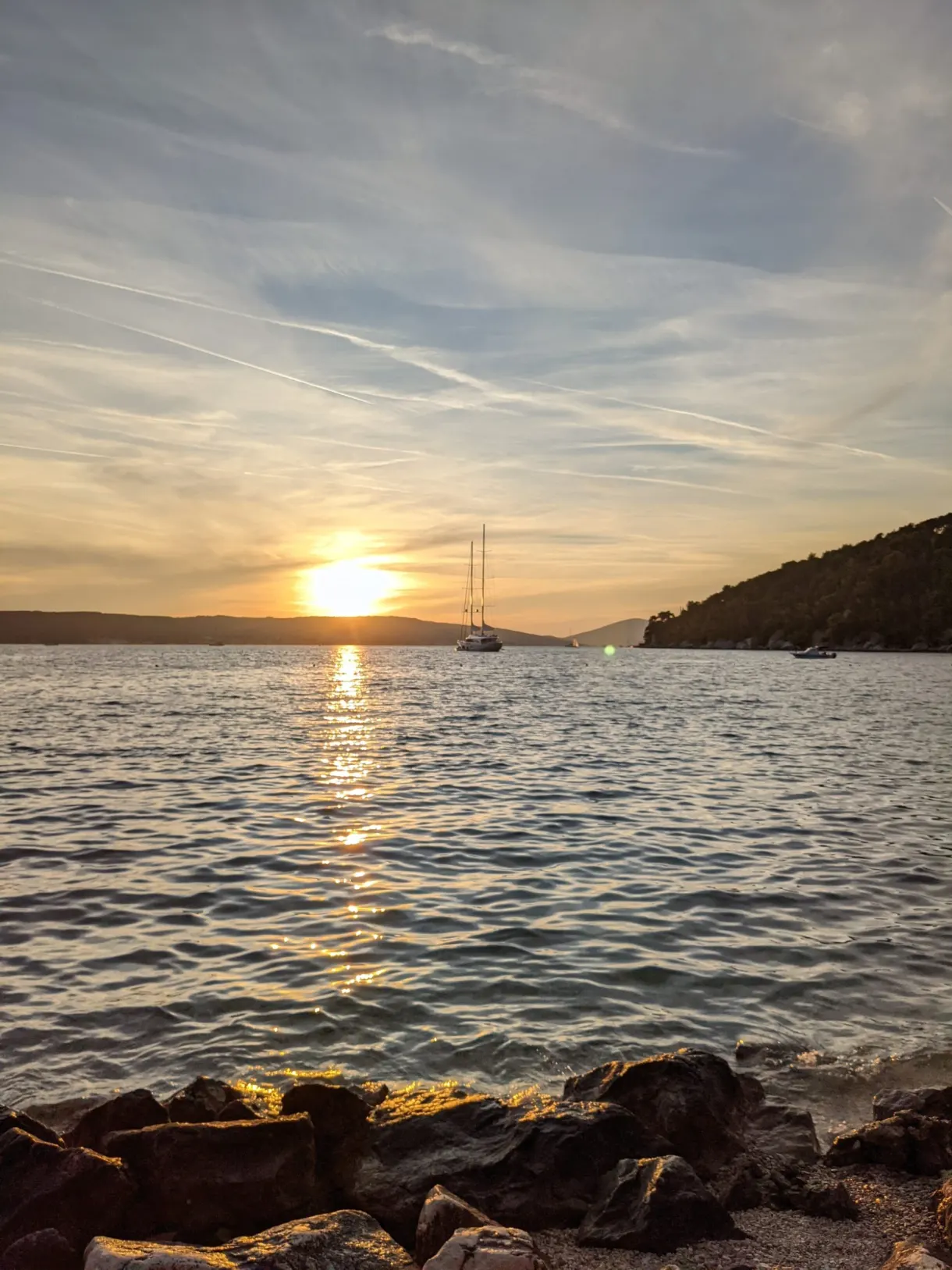 Soleil couchant sur la mer, rochers sombres au premier plan