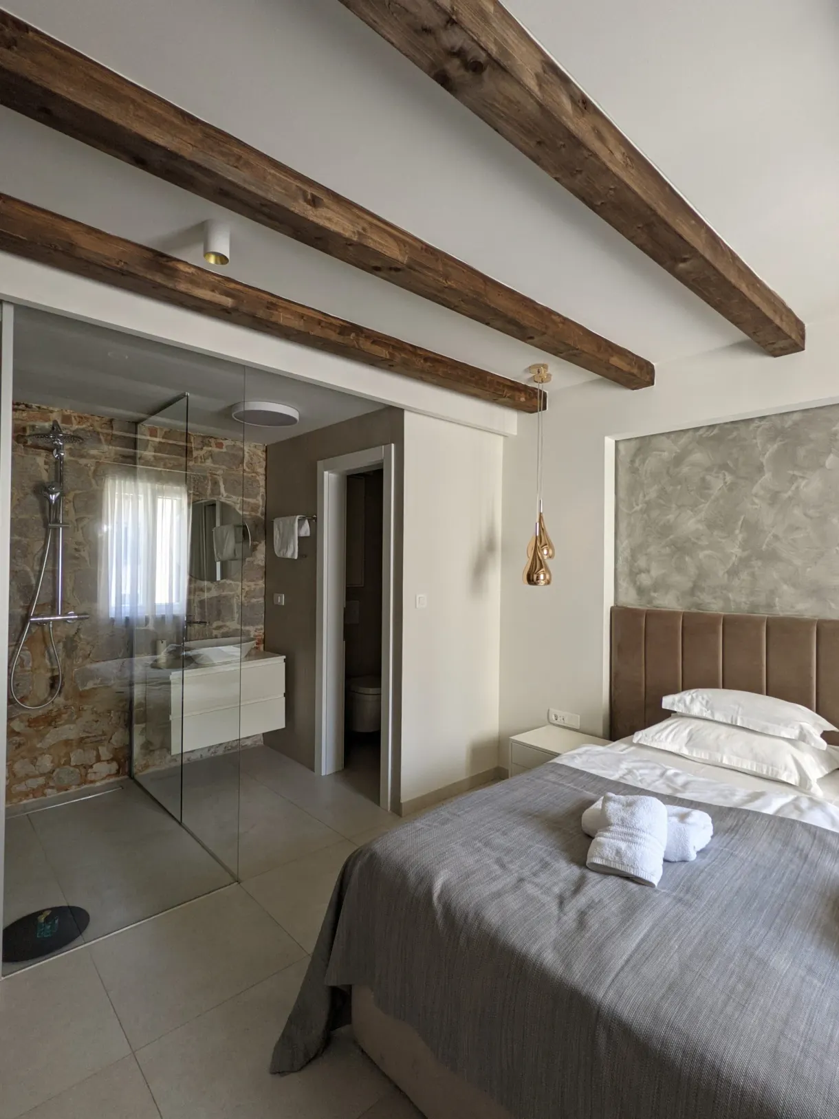 Chambre aux poutres apparentes avec lit blanc et douche vitrée