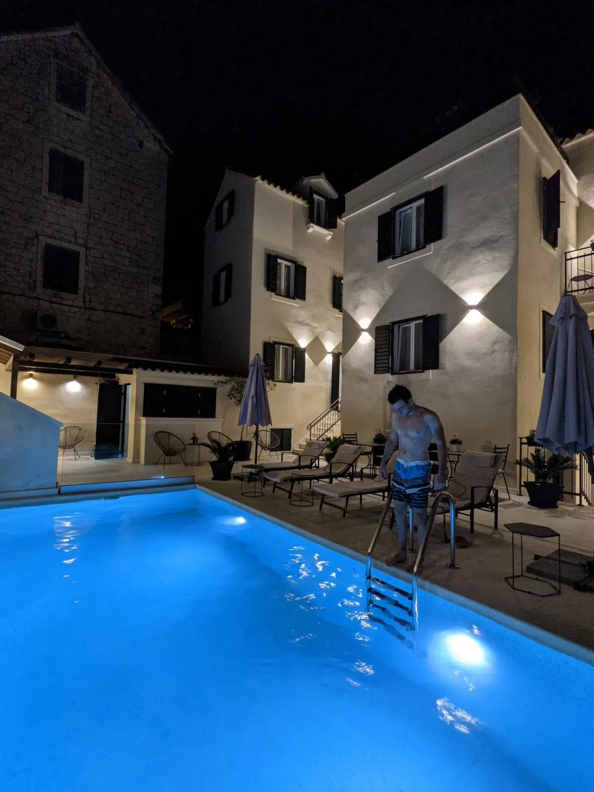 Homme entrant dans une piscine bleue illuminée le soir