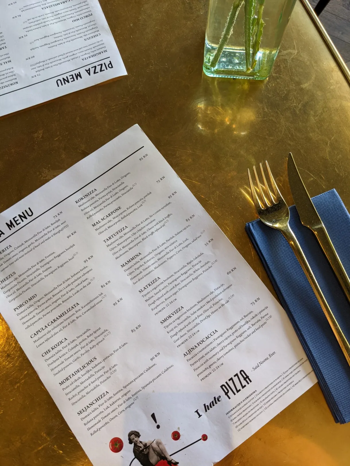 Menu de pizzeria posé sur une table dorée avec couverts