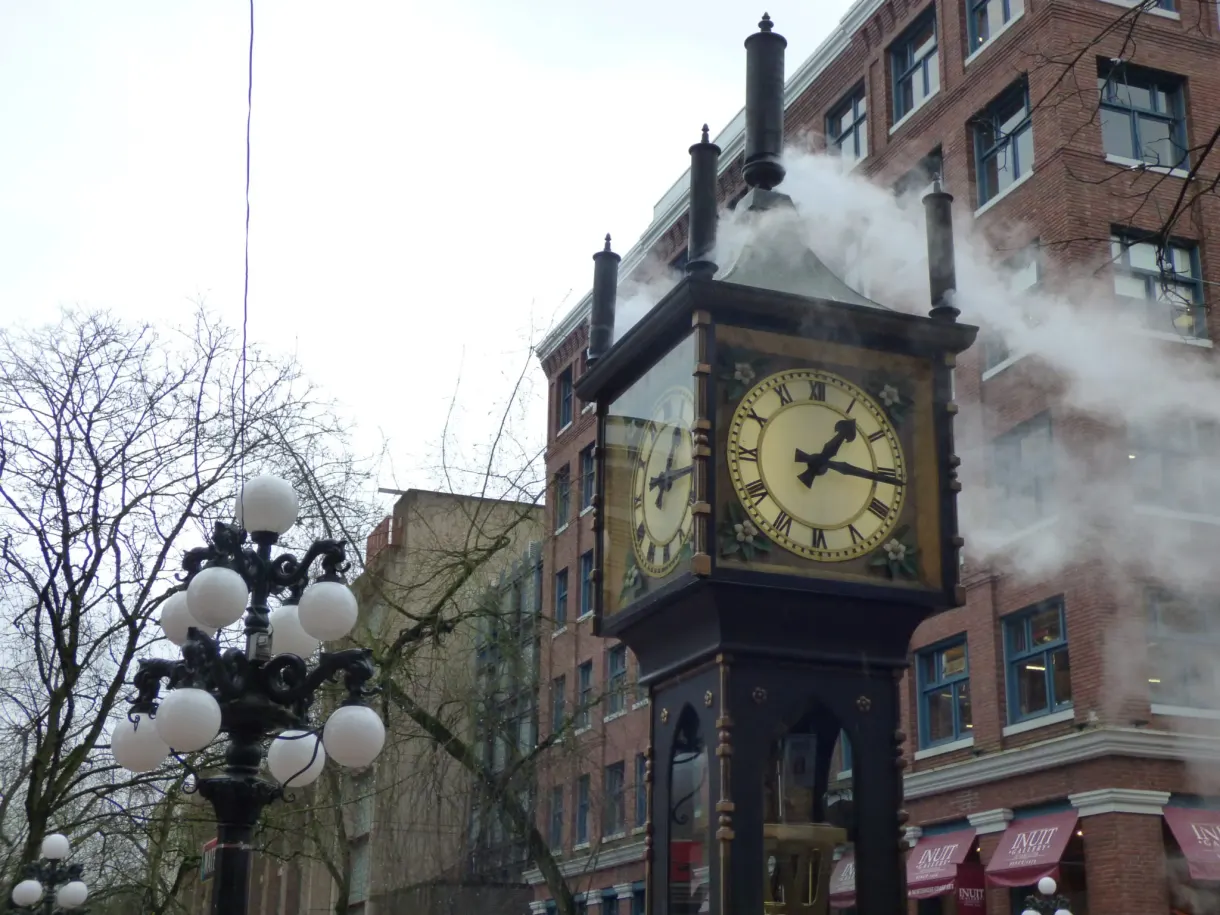 Horloge à vapeur crachant son panache entre les façades de brique