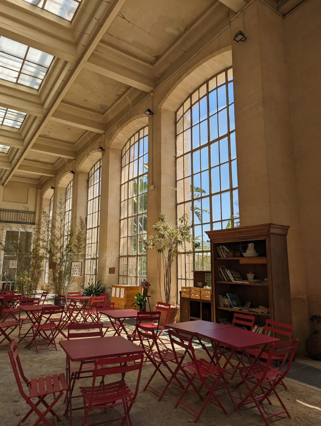 Tables et chaises rouges alignées sous les verrières d'une orangerie