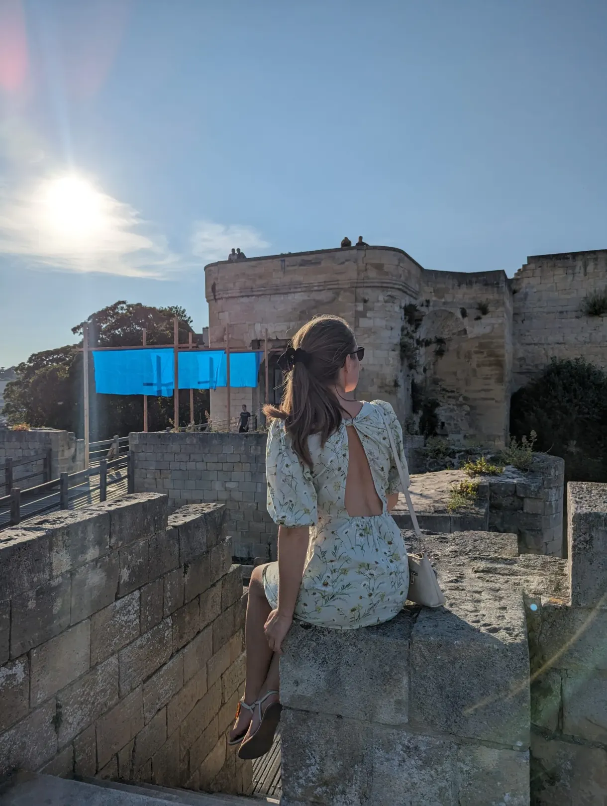 Visiteuse assise sur le rempart de pierre face au soleil