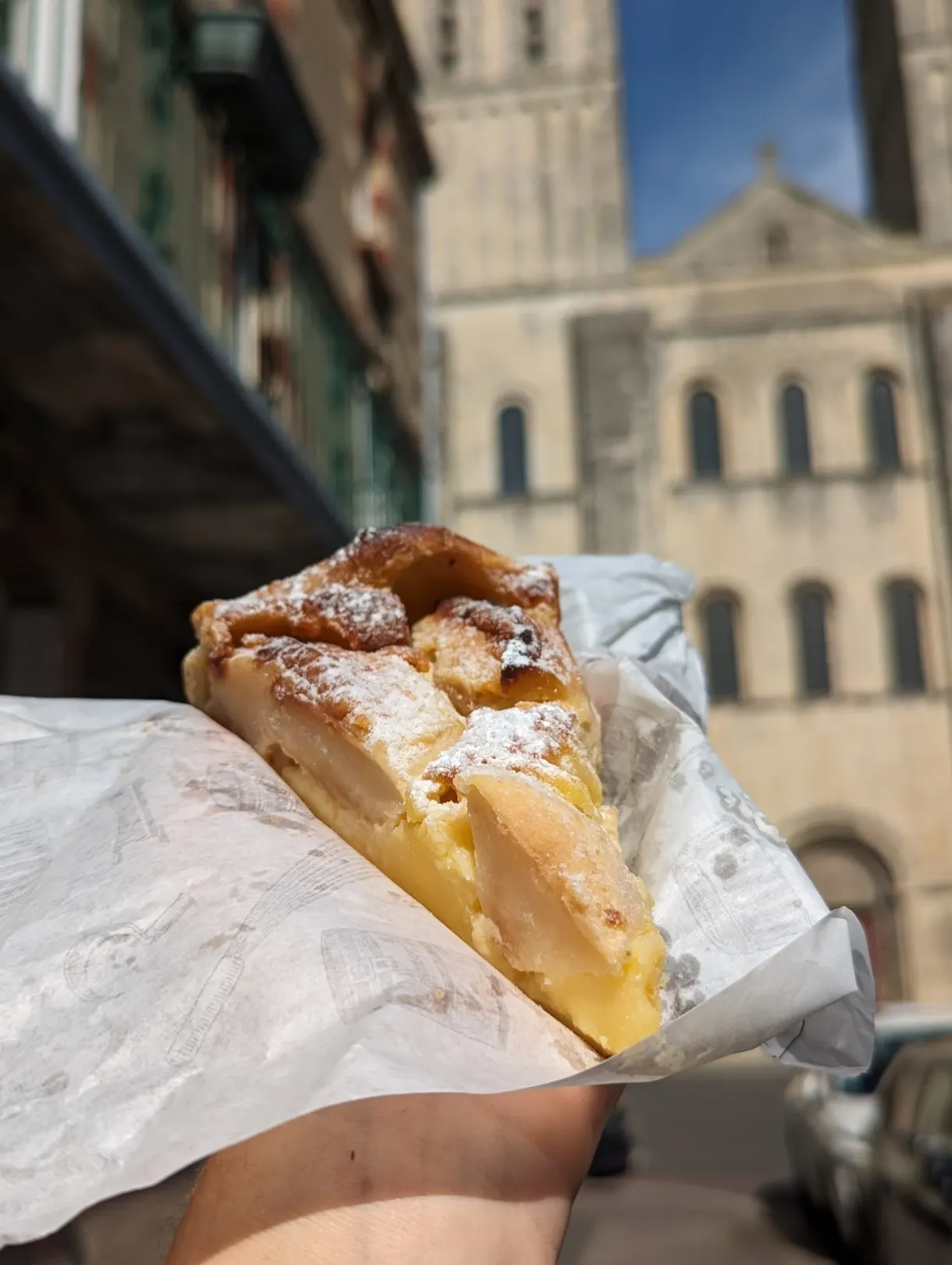 Part de tarte aux pommes tenue à la main devant l'abbatiale