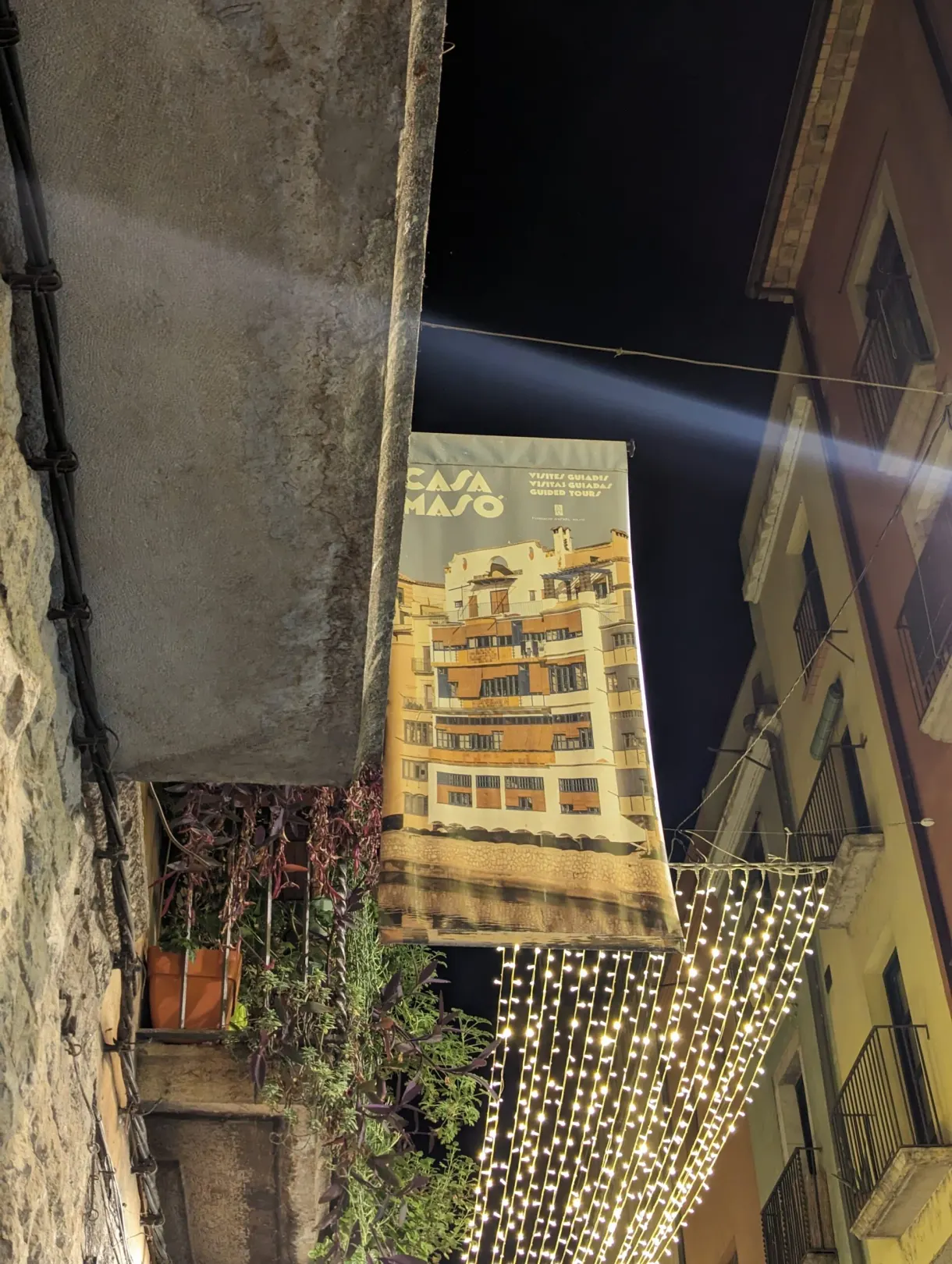 Bannière Casa Masó tendue au-dessus d'une ruelle illuminée de guirlandes
