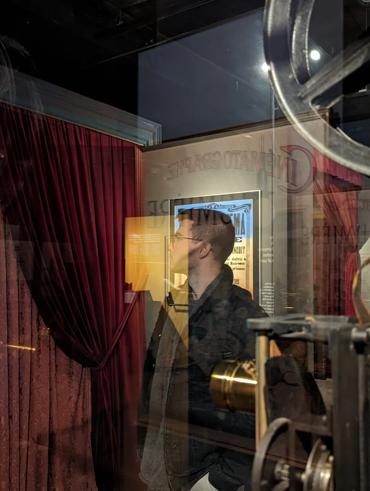 Projecteur de cinéma ancien derrière une vitrine, rideau rouge en fond