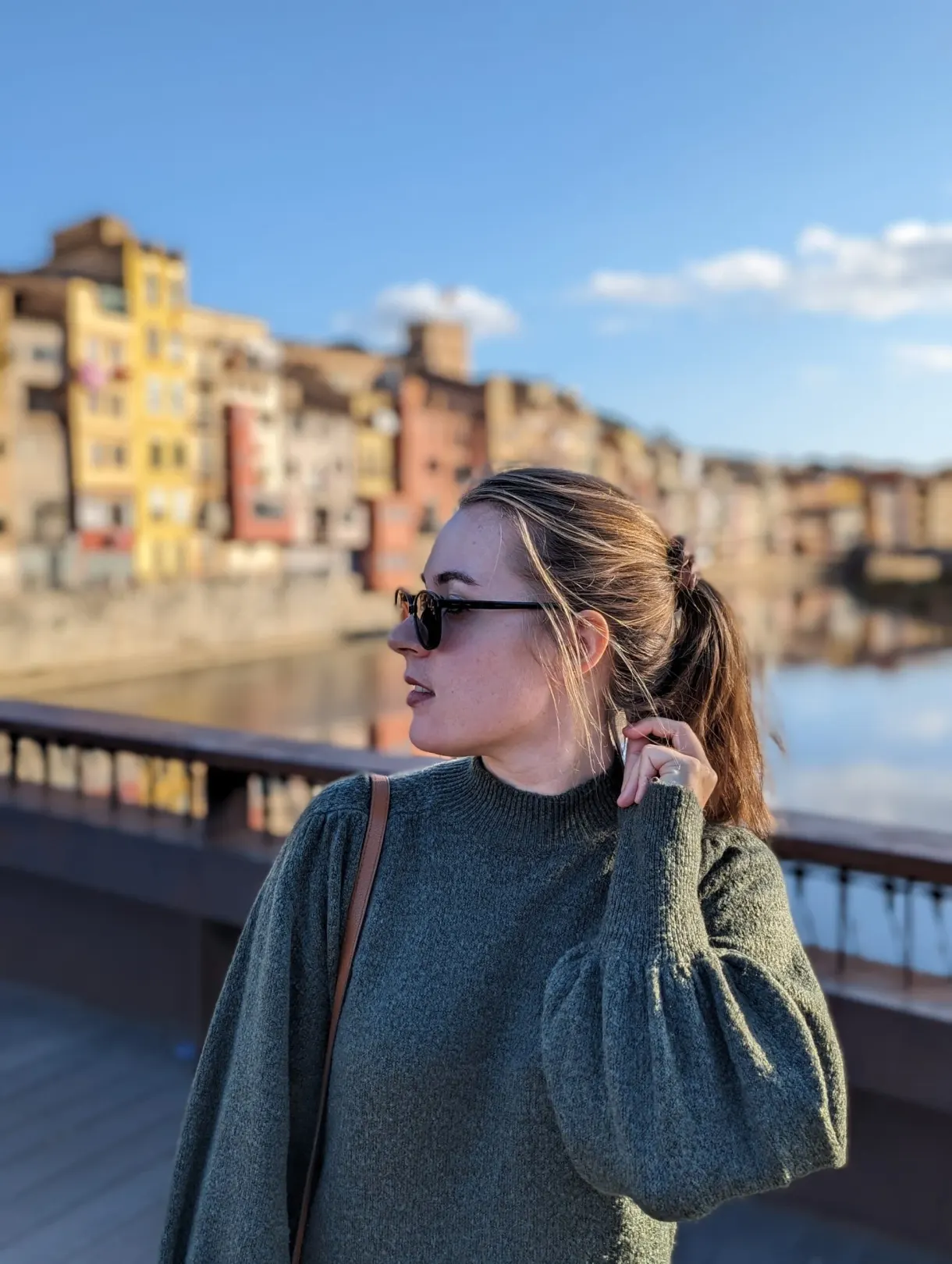 Femme en pull vert sur un pont, maisons colorées derrière elle