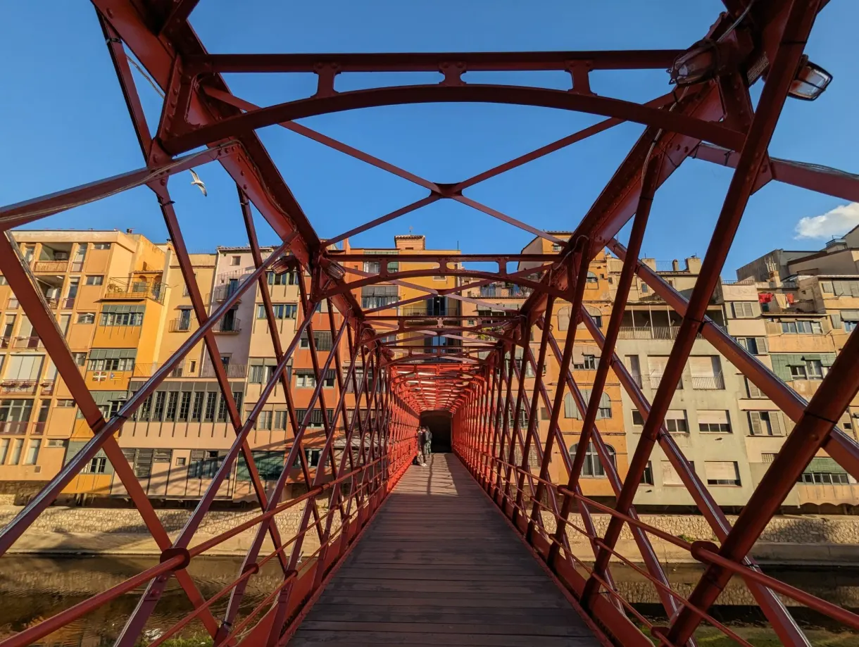 Structure rouge d'une passerelle métallique traversée par un promeneur