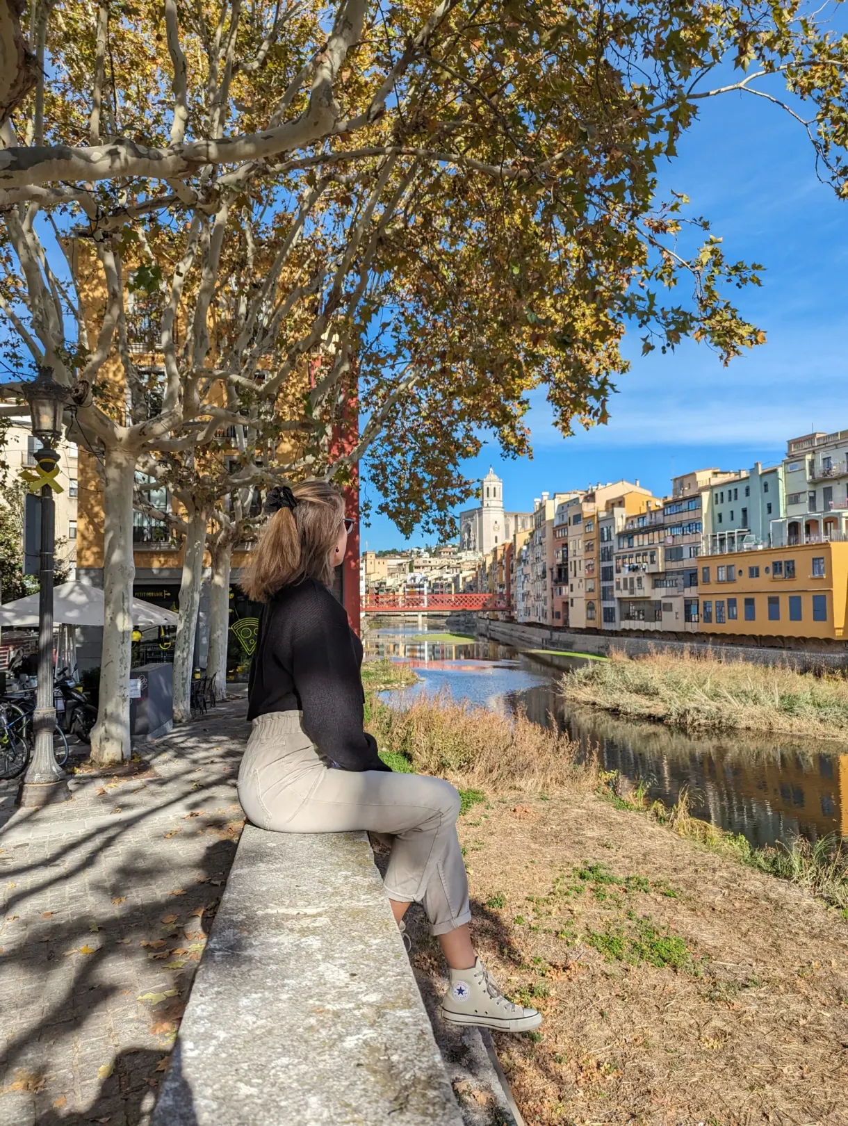 Femme assise sur un muret face à la rivière et aux platanes