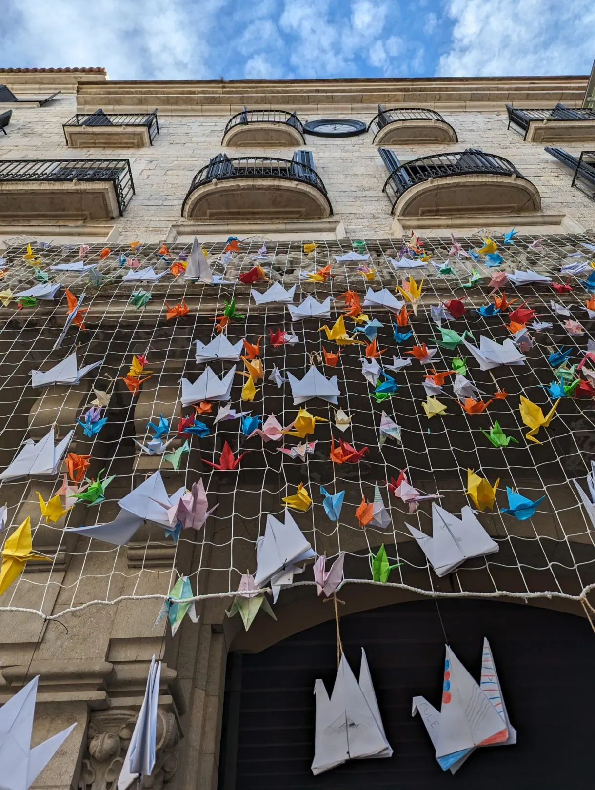 Filet d'origamis colorés tendu devant une façade du centre ancien