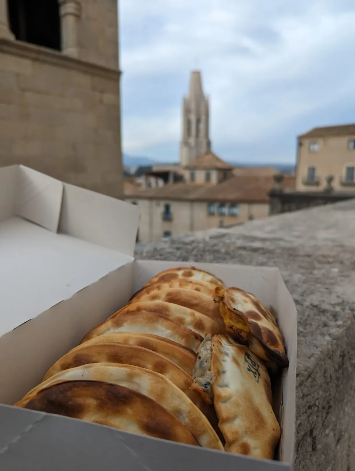 Boîte d'empanadas dorées ouverte face aux toits et au clocher