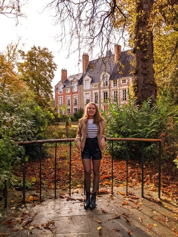 Jeune femme devant la grille du jardin sous les feuilles mortes