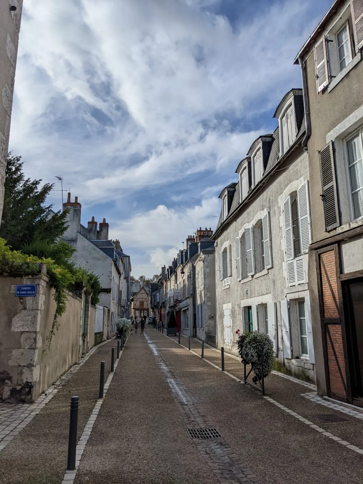 Rue en pente bordée de maisons claires aux volets fermés
